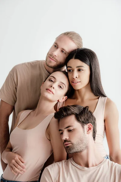 Jóvenes hombres y mujeres multiculturales en traje beige posando juntos aislados en blanco - foto de stock