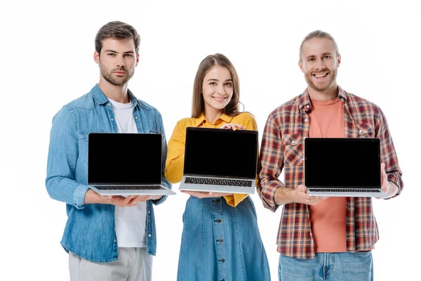 Jóvenes amigos felices sosteniendo computadoras portátiles con pantallas en blanco aisladas en blanco - foto de stock