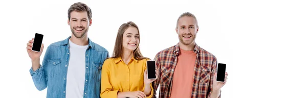 Smiling three young friends holding smartphones with blank screens isolated on white, panoramic shot — Stock Photo