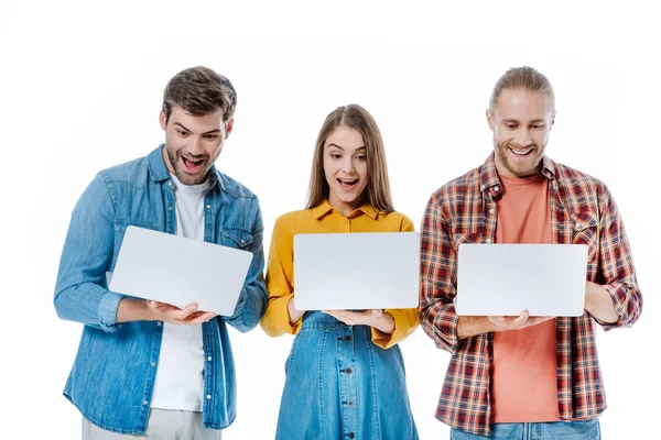 Jóvenes amigos felices sosteniendo computadoras portátiles con bocas abiertas aisladas en blanco - foto de stock