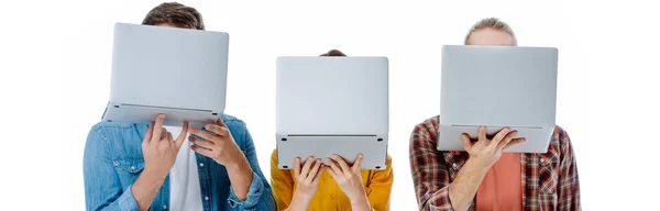 Tres jóvenes amigos sosteniendo ordenadores portátiles en frente de la cara aislado en blanco, plano panorámico - foto de stock