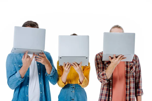 Tres jóvenes amigos sosteniendo ordenadores portátiles en frente de la cara aislado en blanco - foto de stock