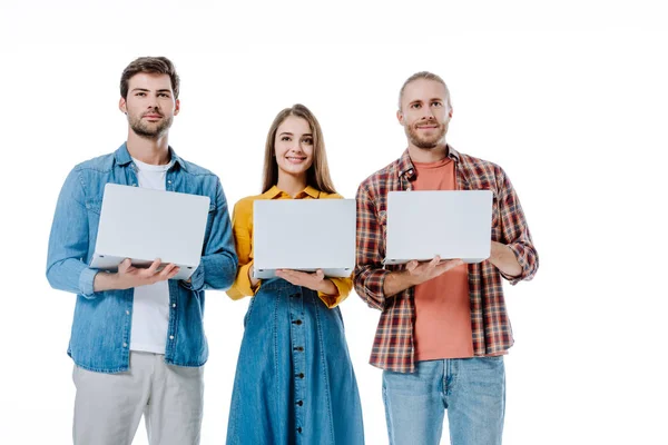 Smiling three young friends holding laptops isolated on white — Stock Photo