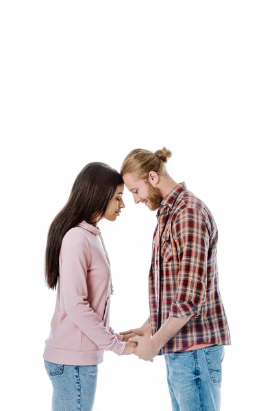 Vista lateral de feliz jovem casal interracial de mãos dadas com os olhos fechados isolados no branco — Fotografia de Stock