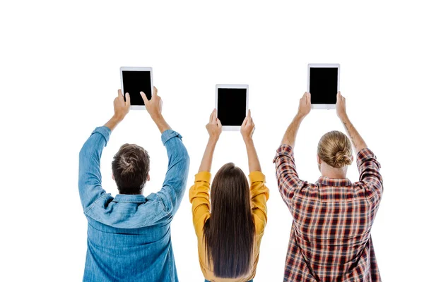 Vista posterior de tres jóvenes amigos sosteniendo tabletas digitales con pantallas en blanco aisladas en blanco - foto de stock