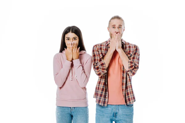Sorprendido joven interracial pareja cubriendo bocas con manos aisladas en blanco - foto de stock