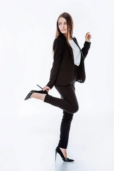 Vista completa de la elegante mujer de negocios en traje posando con la pierna levantada y mirando hacia otro lado aislado en blanco - foto de stock