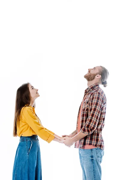 Vista lateral do jovem casal em roupa casual de mãos dadas e olhando para cima isolado no branco — Fotografia de Stock