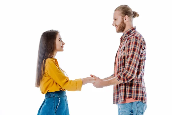 Vista laterale della giovane coppia in abito casual che si tiene per mano e si guarda isolato su bianco — Foto stock