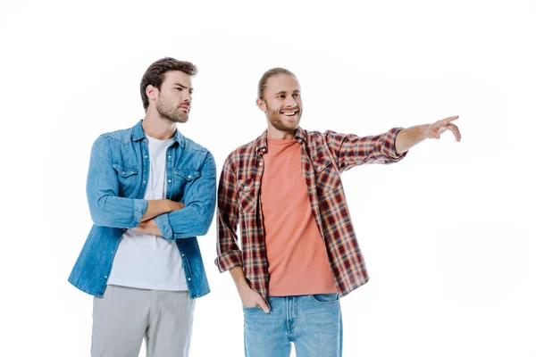 Улыбающийся мужчина, указывающий пальцем, рядом с сосредоточенным другом, изолированным на белом — стоковое фото