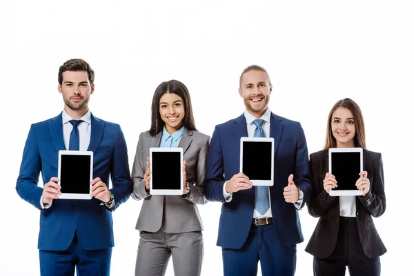 Des hommes d'affaires multiculturels souriants en costumes montrant des tablettes numériques isolées sur blanc — Photo de stock