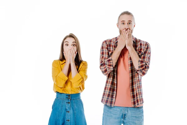 Impactada joven pareja en traje casual cubriendo la boca con las manos aisladas en blanco - foto de stock