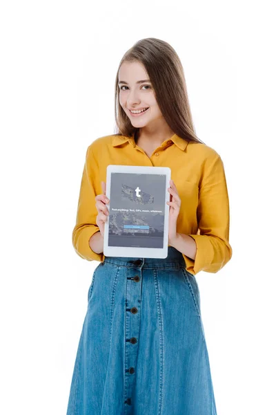 KYIV, UCRANIA - 12 de agosto de 2019: niña sonriente en falda de mezclilla sosteniendo tableta digital con aplicación tumblr aislada en blanco - foto de stock