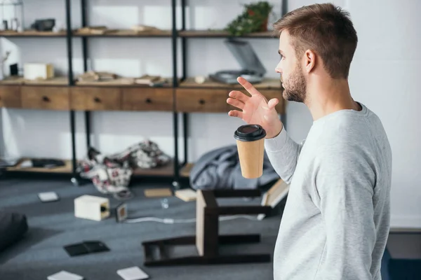 Side view of shocked man dropping paper cup and looking at robbed apartment — Stock Photo