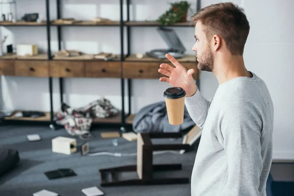 Seitenansicht eines geschockten Mannes, der Pappbecher fallen lässt und auf ausgeraubte Wohnung blickt — Stockfoto