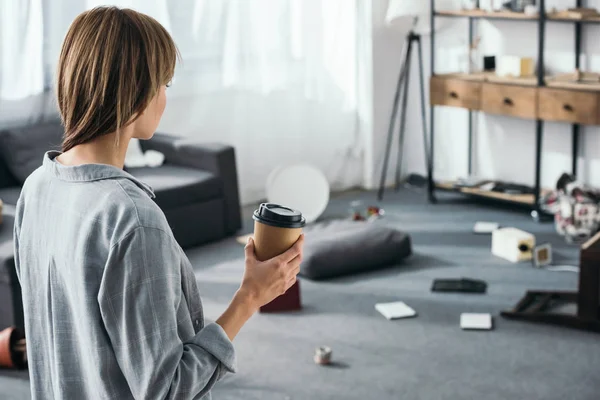 Женщина держит бумажную чашку и смотрит на ограбленную квартиру — стоковое фото
