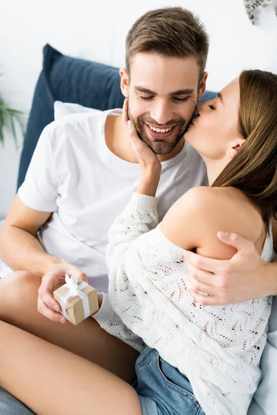 Attractive woman kissing and hugging smiling man with gift — Stock Photo