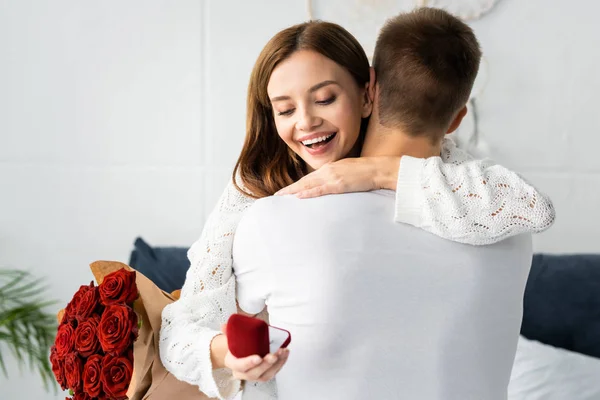 Vista trasera de hombre con ramo y mujer sonriente abrazándolo con caja - foto de stock