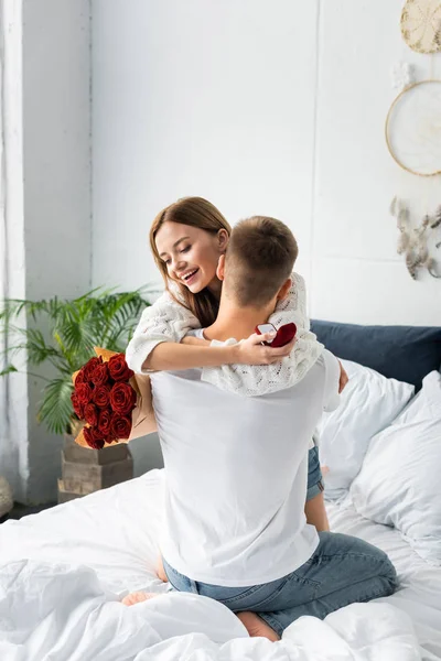 Back view of of man with bouquet and smiling woman hugging him with box — Stock Photo