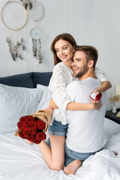 Man with bouquet and smiling woman hugging him with engagement ring — Stock Photo