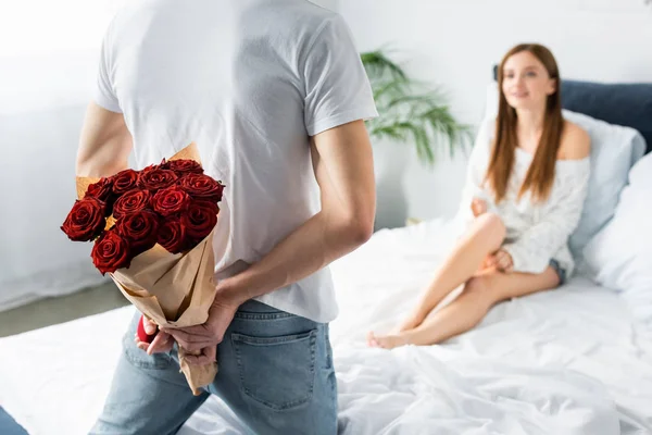 Vista recortada de hombre con ramo y caja y mujer sonriente mirándolo - foto de stock