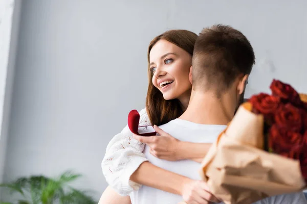 Donna sorridente con anello di fidanzamento e bouquet abbracciando l'uomo — Foto stock