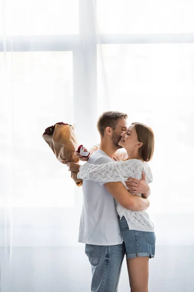 Side view of smiling woman with engagement ring and bouquet hugging man — Stock Photo