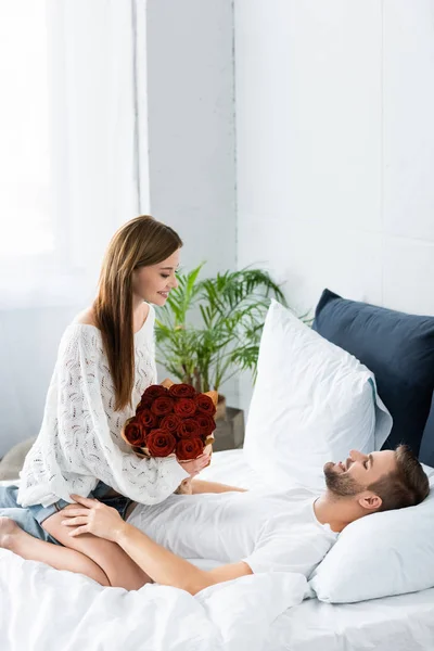 Jolie femme avec bouquet assis sur un homme souriant — Photo de stock