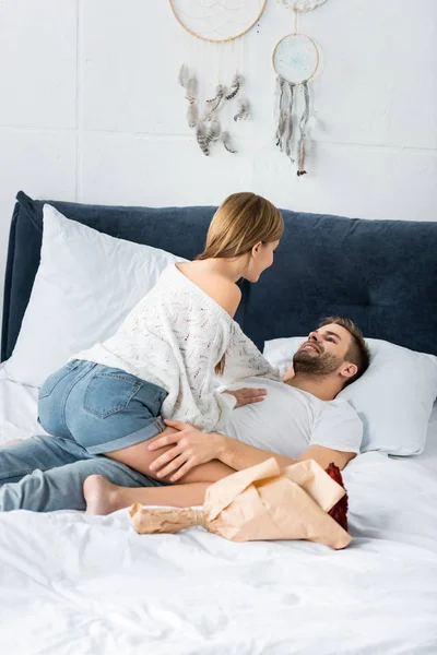 Femme assise sur un homme souriant et beau au lit — Photo de stock