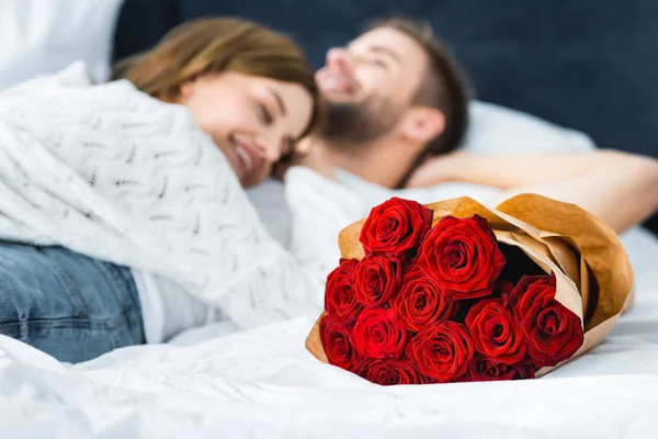 Selective focus of bouquet and woman lying on smiling man on background — Stock Photo