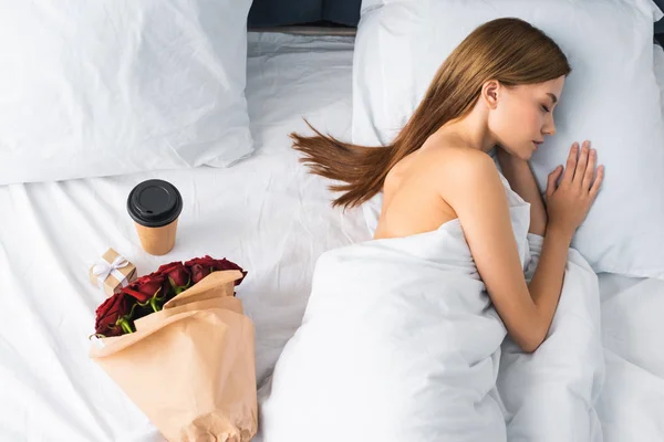 Vista superior de la mujer durmiendo en la cama cerca de la taza de papel y el ramo - foto de stock