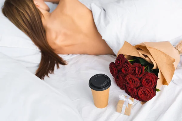 Vista trasera de la mujer durmiendo en la cama cerca de la taza de papel y el ramo - foto de stock