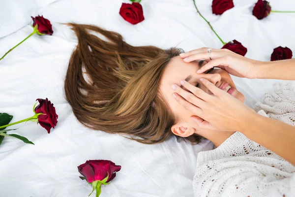 Sonriente mujer oscureciendo la cara y acostada en la cama con rosas - foto de stock