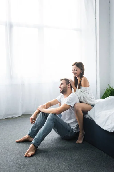 Attractive and smiling woman doing massage of head to handsome man — Stock Photo