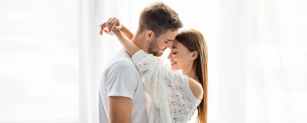 Tiro panorâmico de mulher atraente e sorridente abraçando homem bonito no apartamento — Fotografia de Stock