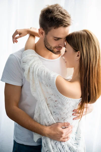 Bonito e sorridente homem abraçando mulher no apartamento — Fotografia de Stock