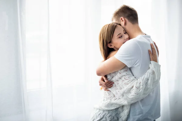 Uomo che abbraccia donna attraente e sorridente in appartamento — Foto stock