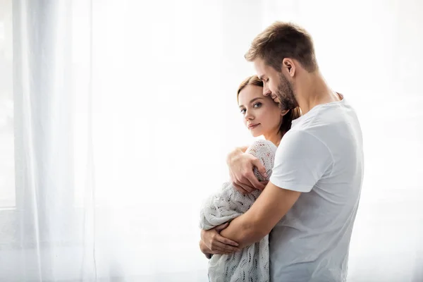 Hombre guapo abrazando a mujer atractiva en apartamento - foto de stock