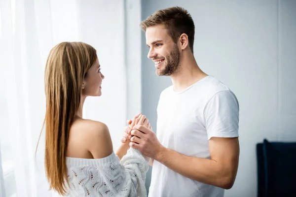 Hombre guapo cogido de la mano con la mujer sonriente en el apartamento - foto de stock