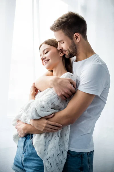 Hombre guapo abrazando mujer atractiva y sonriente en el apartamento - foto de stock