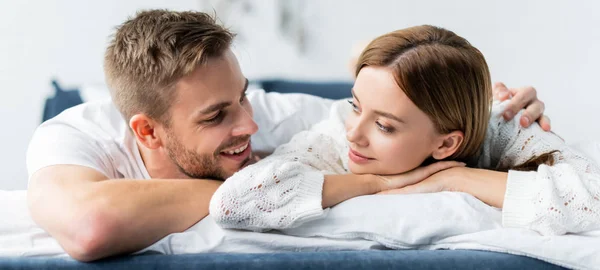 Plano panorámico de hombre guapo abrazando a mujer atractiva y sonriente en apartamento - foto de stock