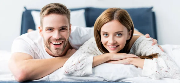 Panoramic shot of handsome man hugging attractive and smiling woman in apartment — Stock Photo