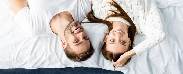 Panoramic shot of handsome man and smiling woman looking at camera in apartment — Stock Photo