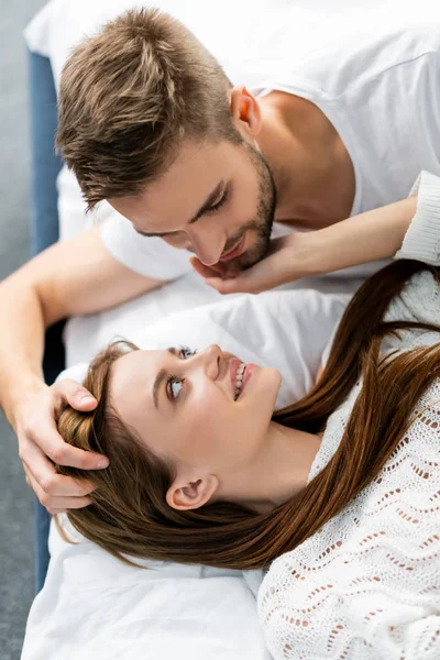 Vista aérea del hombre guapo abrazando mujer atractiva y sonriente en el apartamento - foto de stock