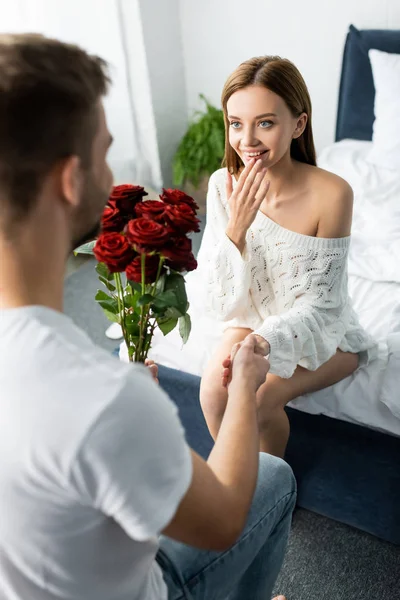 Cropped view of man giving bouquet to attractive and shocked woman in apartment — Stock Photo