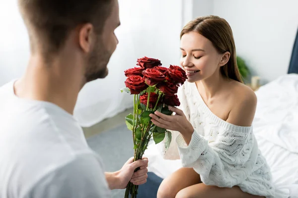 Abgeschnittene Ansicht von Mann gibt Blumenstrauß an attraktive und lächelnde Frau in Wohnung — Stockfoto