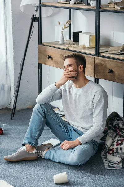 Handsome and shocked man obscuring face in robbed apartment — Stock Photo