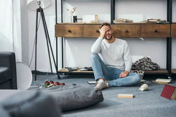 Schöner und schockierter Mann verdeckt Gesicht in beraubter Wohnung — Stockfoto