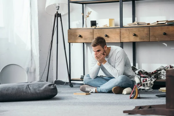 Handsome and shocked man obscuring face in robbed apartment — Stock Photo