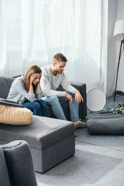 Sad woman and handsome man sitting on sofa in robbed apartment — Stock Photo